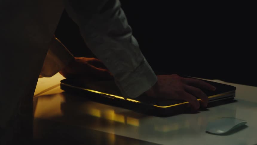 An abstract glitch effect shows hands frantically pressing down on a glowing laptop in a dark room