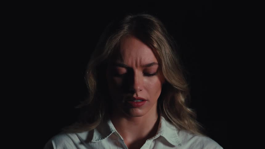 Dramatic close-up of a blonde woman's face showing fear and shock as she looks into the camera against a black background