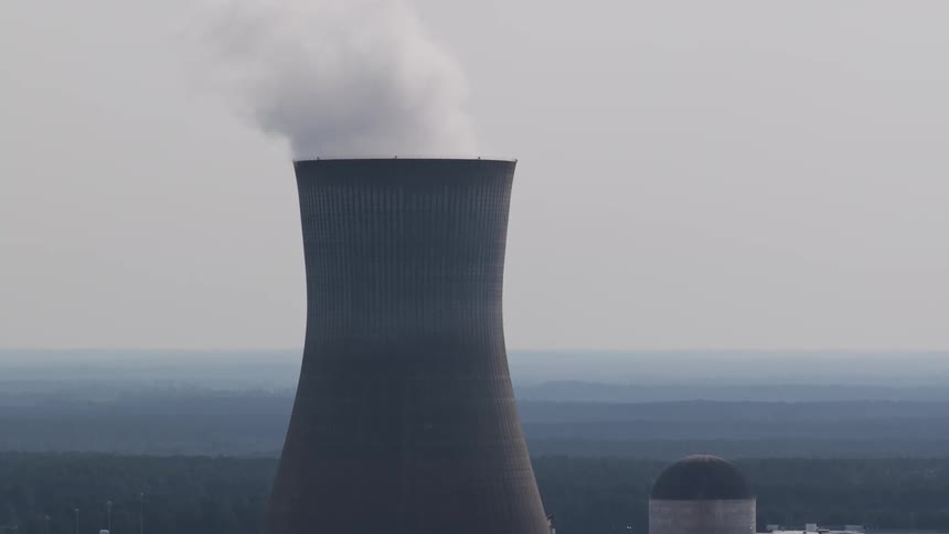 A nuclear power plant's cooling tower releases steam into the grey sky as the camera tilts up