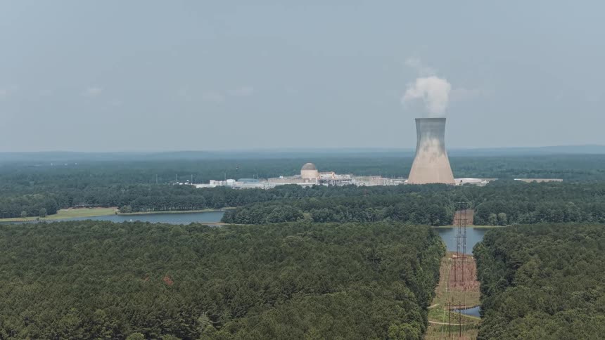 Slow aerial tilt-up reveals the Shearon Harris Nuclear Power Plant and its cooling tower over a dense forest, with power lines leading the way