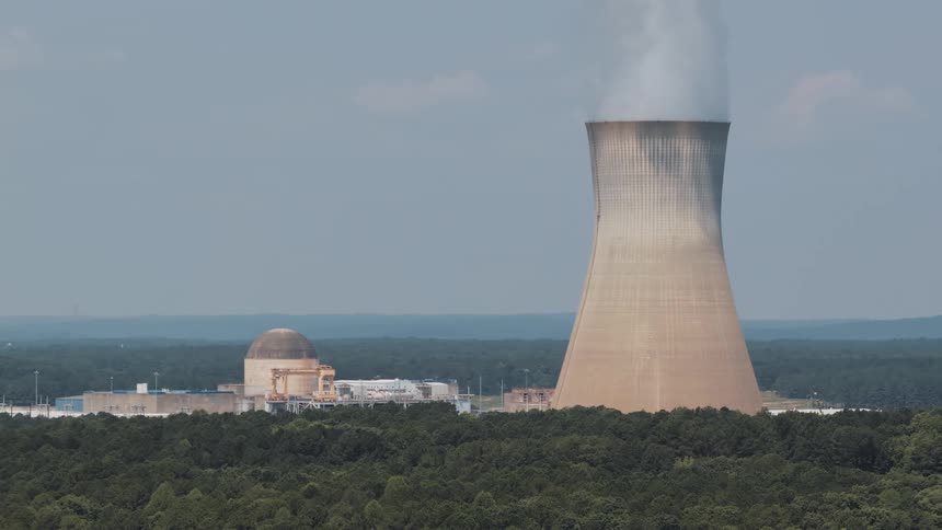 A nuclear power plant with its cooling tower emitting steam, set against a backdrop of a dense forest and a hazy sky