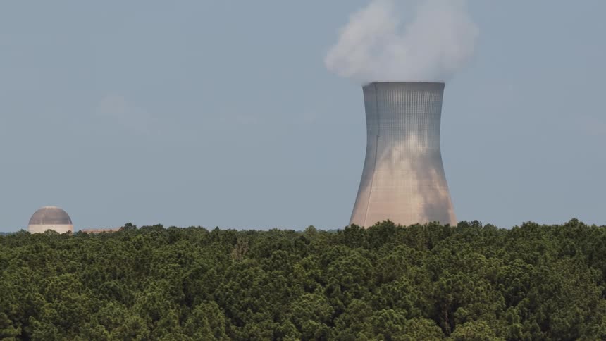 Aerial shot pulls back from a steaming nuclear cooling tower to reveal the entire power plant complex surrounded by lush trees