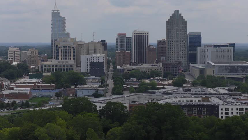 A slow aerial pullback reveals the downtown Raleigh, North Carolina skyline and surrounding urban landscape on an overcast day