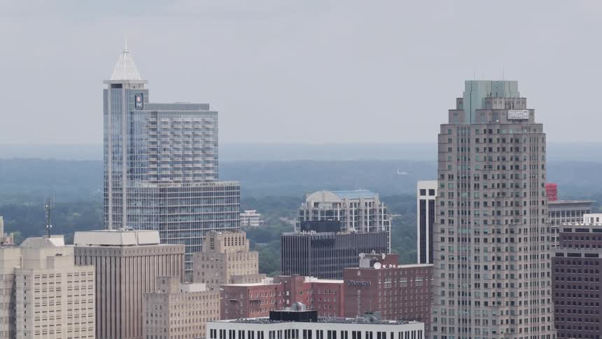 A slow zoom out from a hazy city skyline showcases various skyscrapers as an airplane flies in the distant sky