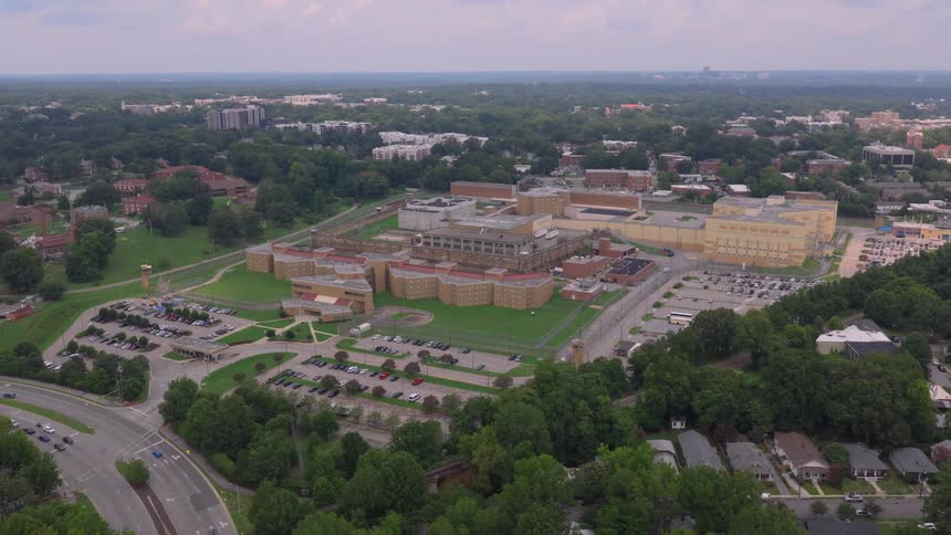 A slow revealing aerial shot of a large state prison and correctional facility complex surrounded by a suburban neighborhood