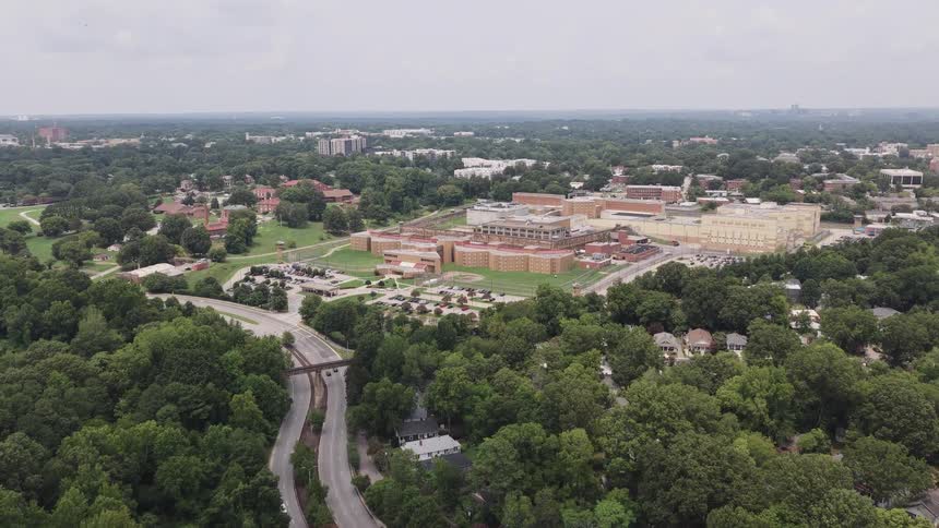 A slow aerial pullback reveals a large state prison complex situated within a lush, green suburban landscape