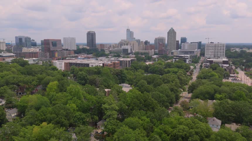 Slow aerial reveal of the Raleigh, North Carolina city skyline, rising above the trees of a quiet suburban neighborhood