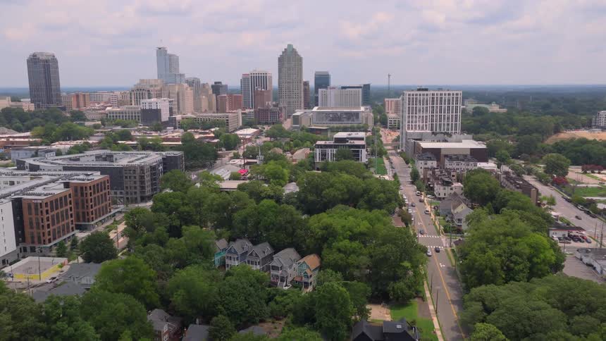 Aerial drone view flying over a lush green residential neighborhood towards the downtown city skyline of Raleigh, North Carolina