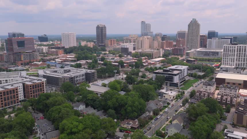 An aerial view slowly pulls back from the Raleigh, North Carolina skyline, revealing the lush green trees of the surrounding residential neighborhoods