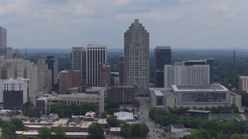 Aerial tracking shot of the downtown Raleigh, North Carolina skyline with modern architecture under a cloudy sky