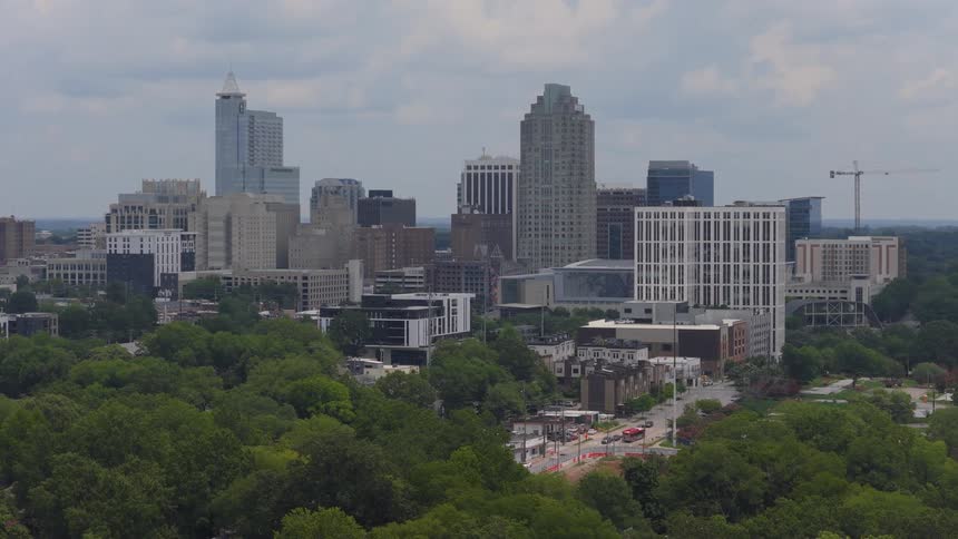 Slow zoom aerial of the downtown Raleigh, North Carolina skyline rising above a lush green park on an overcast day