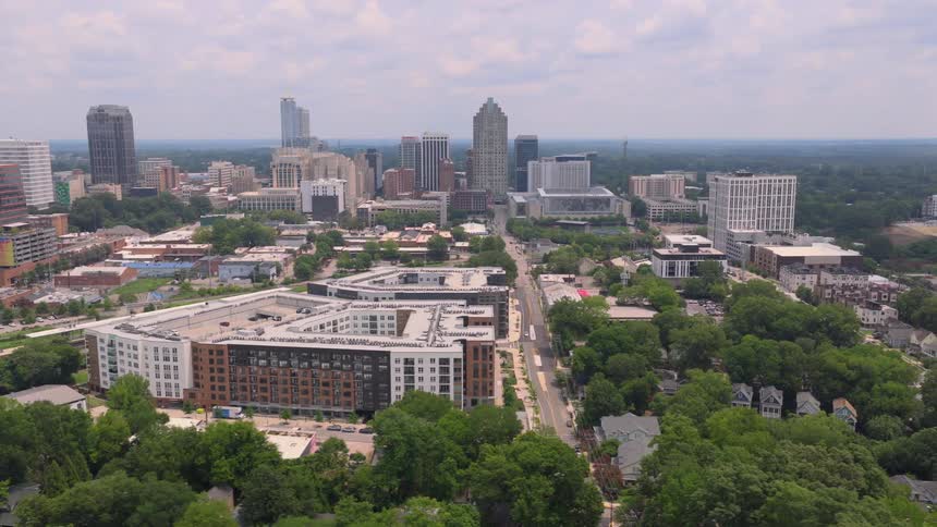 A slow aerial reveal of a modern city skyline, showing a mix of residential apartments and skyscrapers surrounded by green trees