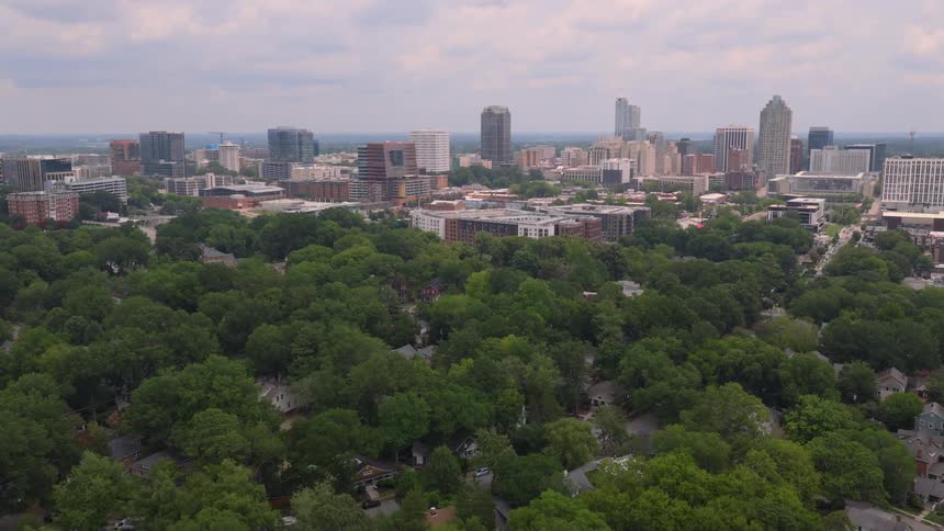 A slow aerial push-in shot over a lush green residential neighborhood towards the Raleigh, North Carolina skyline