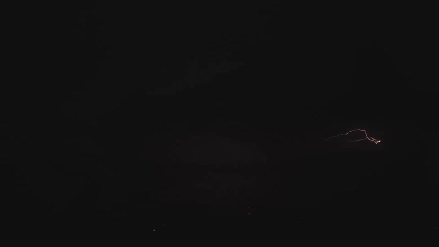 A dramatic slow-motion shot captures a powerful bolt of lightning spreading across the dark, stormy night sky