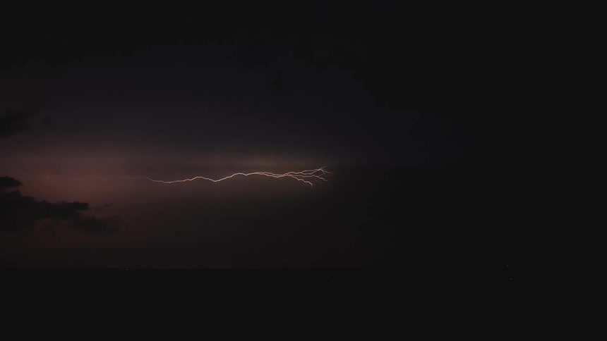 A powerful bolt of lightning streaks horizontally across the dark sky during a nighttime thunderstorm