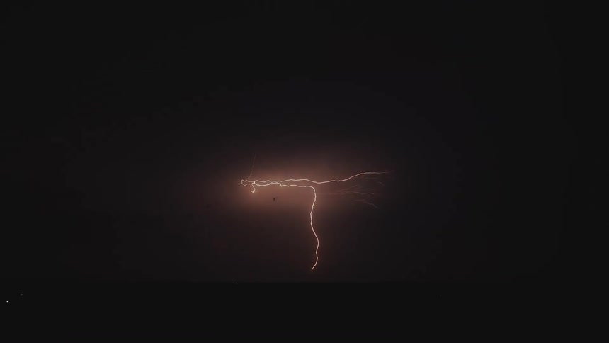 A single, powerful lightning bolt illuminates the stormy night sky over a flat horizon in slow motion