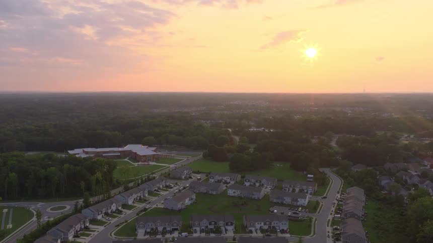 The setting sun casts a beautiful golden glow over a quiet suburban housing development nestled among green trees