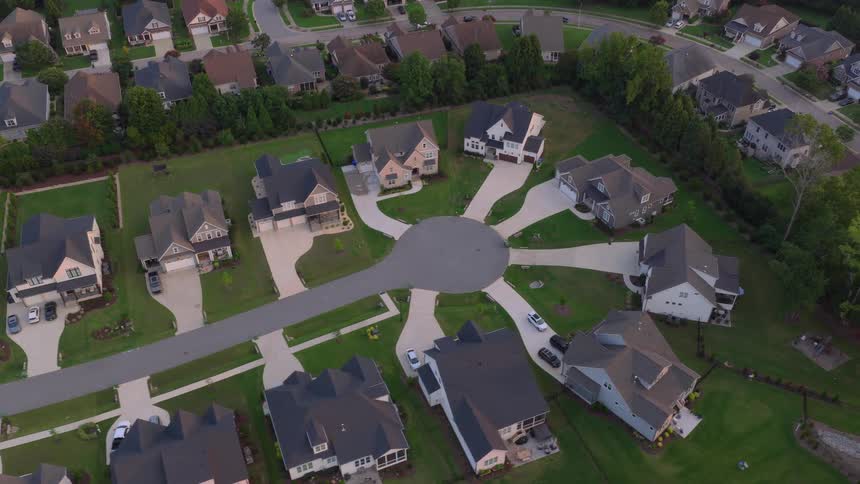 A slow ascending high-angle drone shot reveals an idyllic suburban cul-de-sac community with large family homes at sunrise