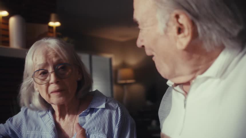 A senior couple experiences a moment of relief and joy while calculating their bills and finances together at their home table in the evening