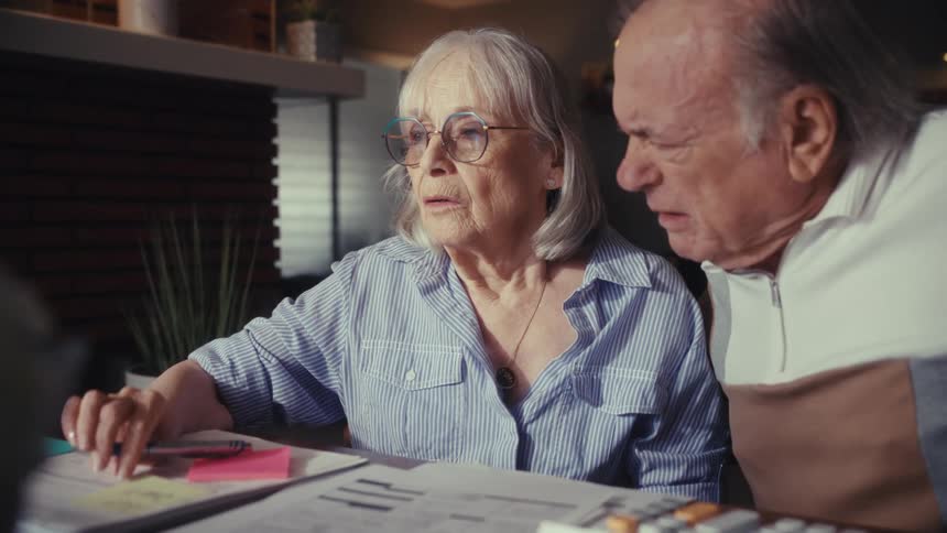A stressed senior couple reviews their finances together at home, looking shocked and worried by the results of their calculations