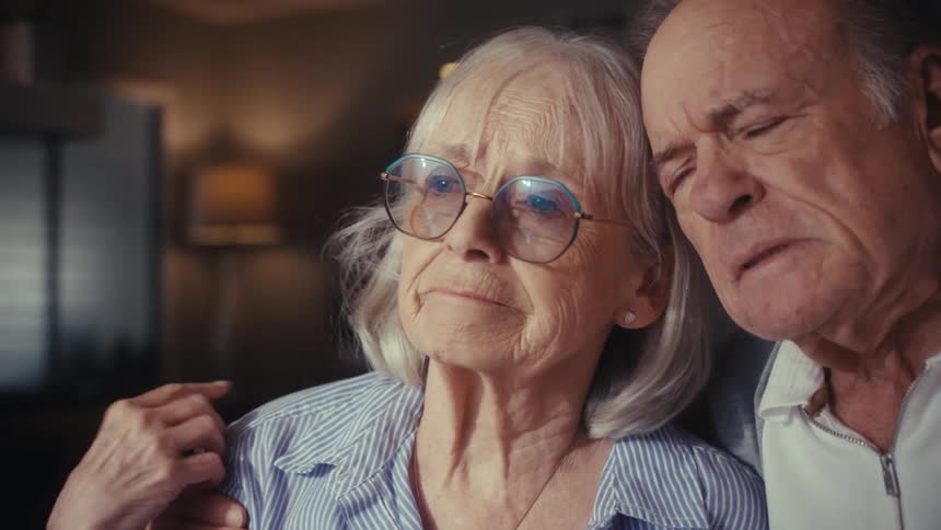 A worried elderly couple reviews their finances with a calculator at home, finding comfort and support in each other during a stressful moment