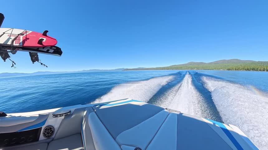 A wide-angle, point-of-view shot from the back of a speedboat as it races in slow motion across a vast blue lake on a sunny day