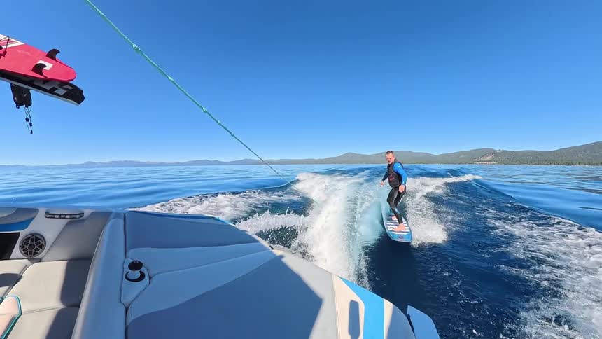 Slow motion shot of a man wakesurfing behind a boat on a vast, beautiful blue lake under a clear sky