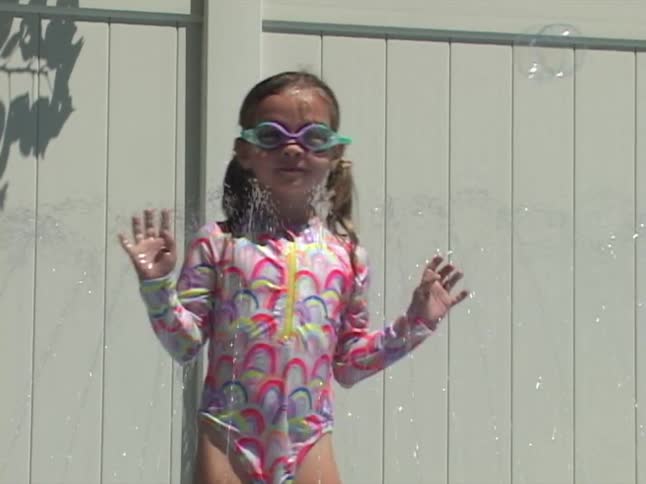 Young girl in goggles splashes and plays with bubbles in a backyard kiddie pool on a sunny day