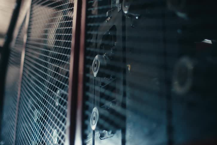 Close-up of an industrial machine with spinning rollers processing thin wire behind a protective mesh