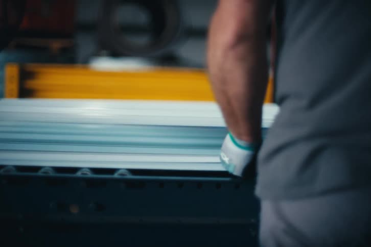 Blurred view of a male worker's arm guiding long materials on a factory production line