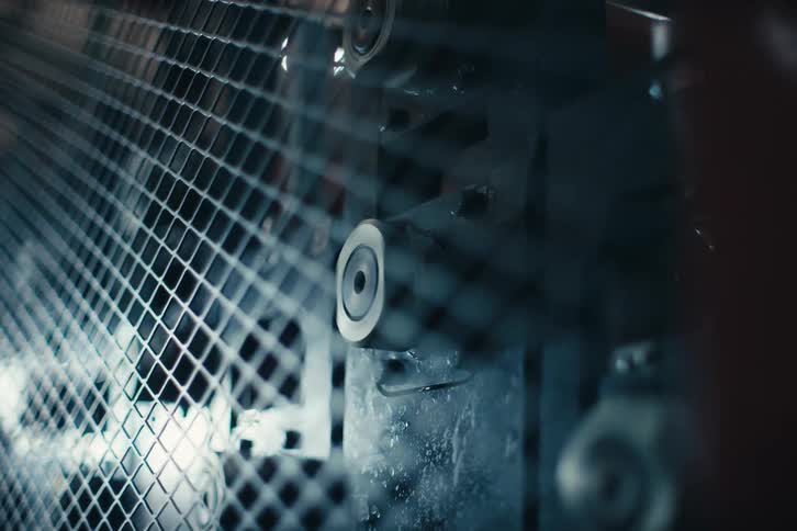 Close-up of industrial rollers spinning behind a protective metal grid in a factory setting