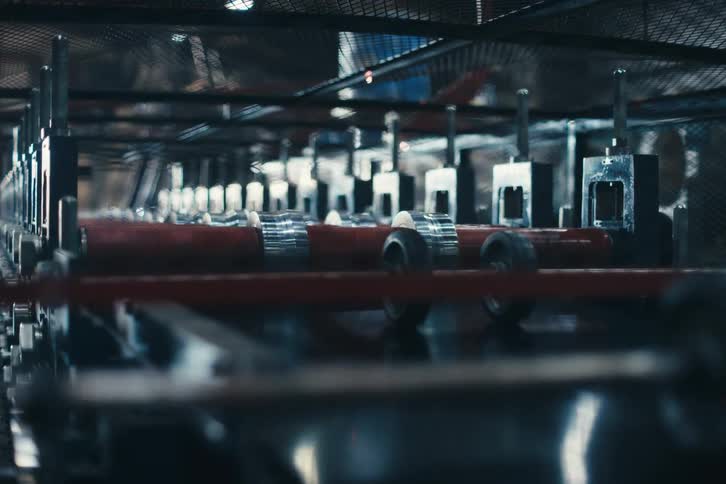 A slow dolly back reveals an automated assembly line with rollers spinning inside an industrial manufacturing plant