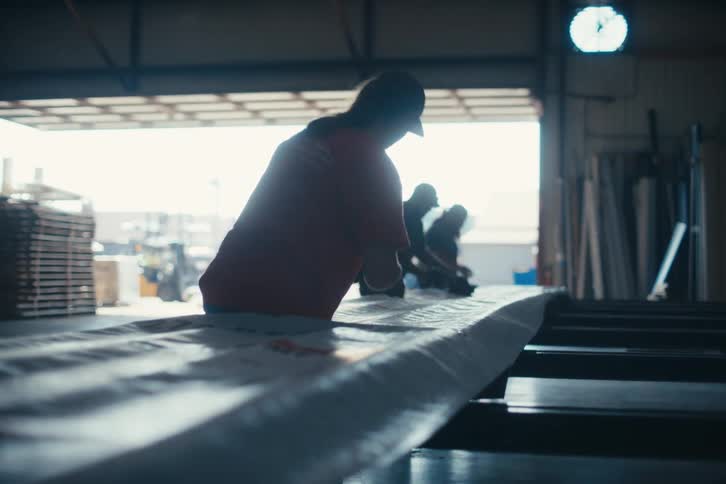 A team of workers diligently crafts products on a production line inside a sunlit manufacturing warehouse