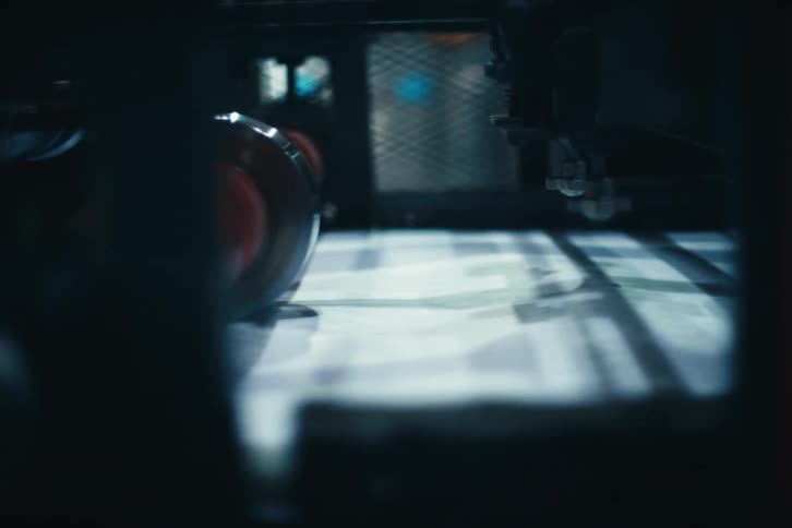 A moody close-up shot captures newspapers moving at high speed through an industrial printing press