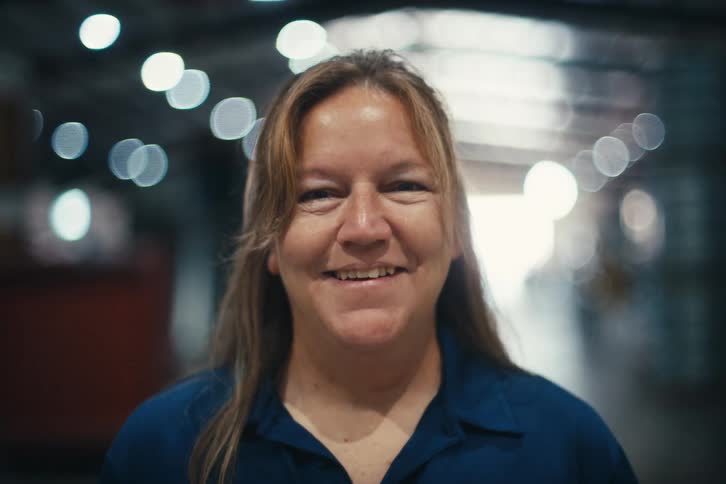 Portrait of a smiling female factory worker looking at the camera in a warehouse with bokeh lights