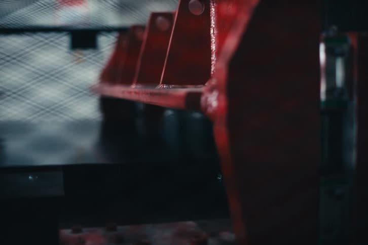 Close-up slow pan across a large, red industrial machine inside a manufacturing facility with a hearing protection sign blurred in the foreground