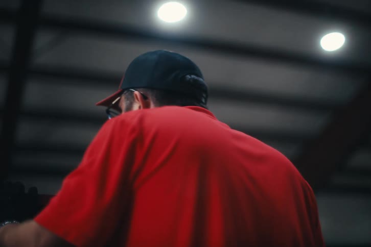 A slow-motion cinematic shot follows a bearded factory worker in a red shirt as he operates an industrial machine's control panel