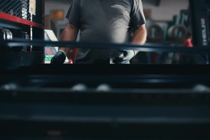 In a bustling factory, a skilled worker carefully guides freshly formed metal roofing panels along a modern conveyor belt system