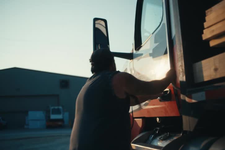 A truck driver walks to his semi-truck at sunrise, gets in the cab, and shuts the door to begin his day in slow motion