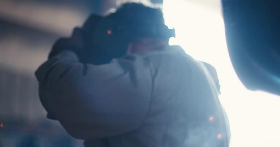 Slow-motion close-up of a welder in a protective mask, with brilliant sparks flying as they work in a factory