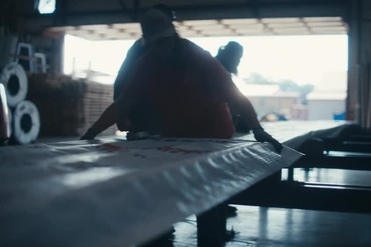 Silhouetted factory workers collaborate on a production line inside a large industrial warehouse