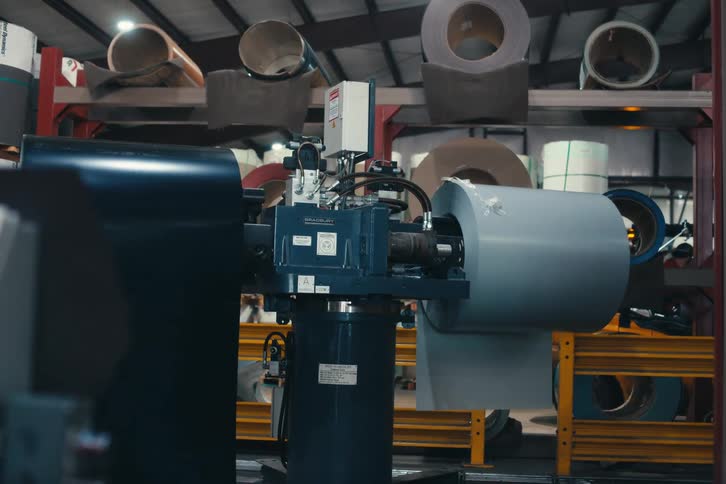 Large roll of sheet metal uncoiling from an industrial machine in a manufacturing plant