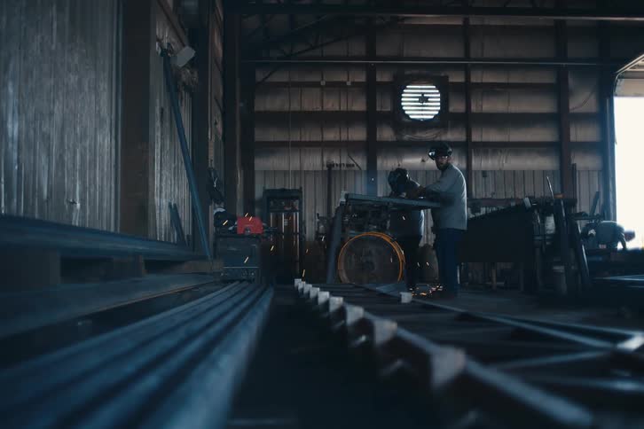 A welder works diligently in a large industrial workshop, with bright sparks flying as he joins metal parts