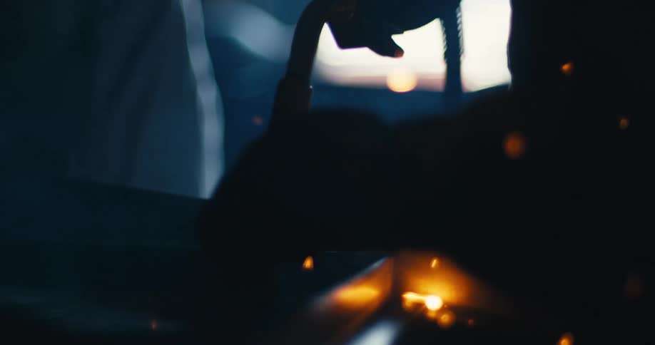 Slow-motion close-up of a welding torch creating a shower of bright sparks as it fuses metal in a dark industrial setting
