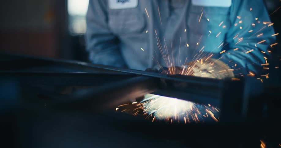 Close up slow motion shot of a welder joining two metal beams, creating a dramatic shower of sparks in a workshop
