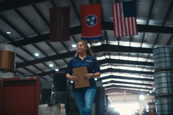 A proud woman with a clipboard walks in slow motion through a large metal manufacturing warehouse
