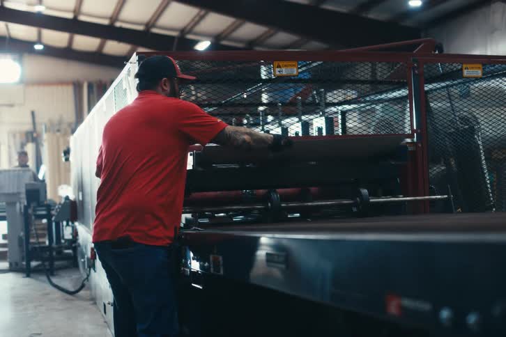 Male factory worker in a red shirt operates a large industrial processing machine in a warehouse