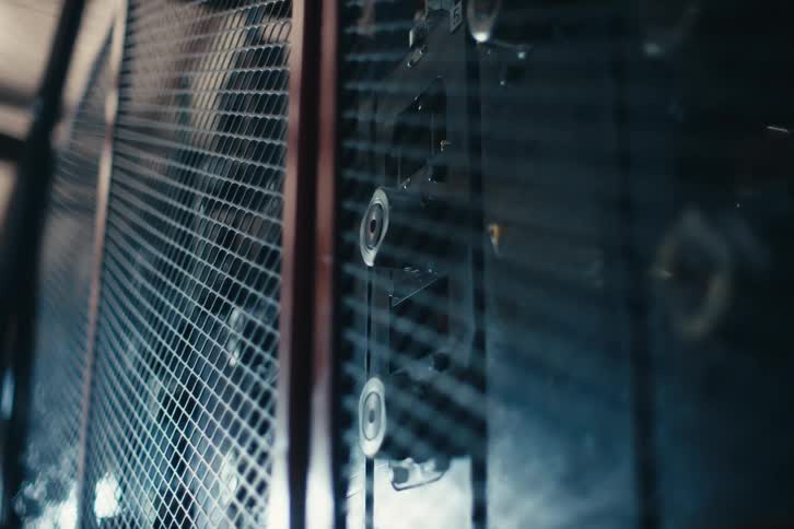 A close-up shot of a dark industrial machine operating behind a wire mesh safety guard