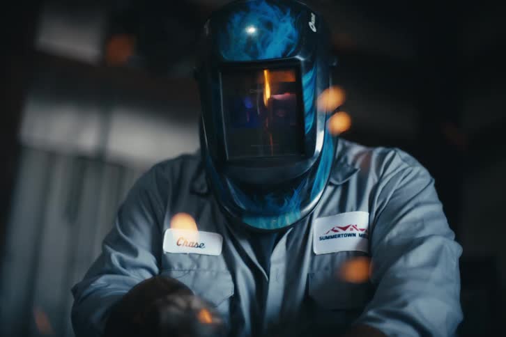 A focused welder in a protective mask works diligently as bright orange sparks fly in a workshop