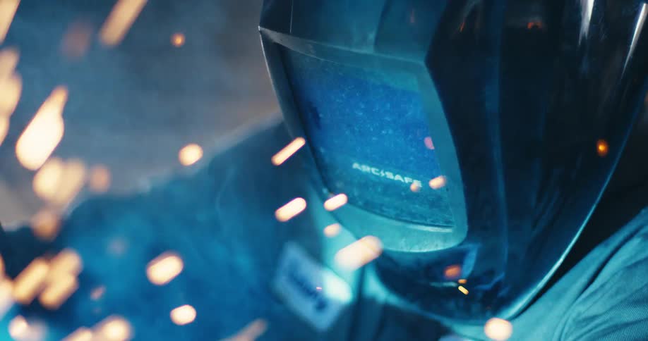 Slow motion close-up of a welder's helmet as bright sparks fly around